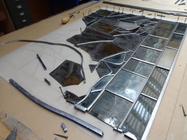 A panel during assembly – note the design attached to the board below the glass, and the nails holding the pieces in place.